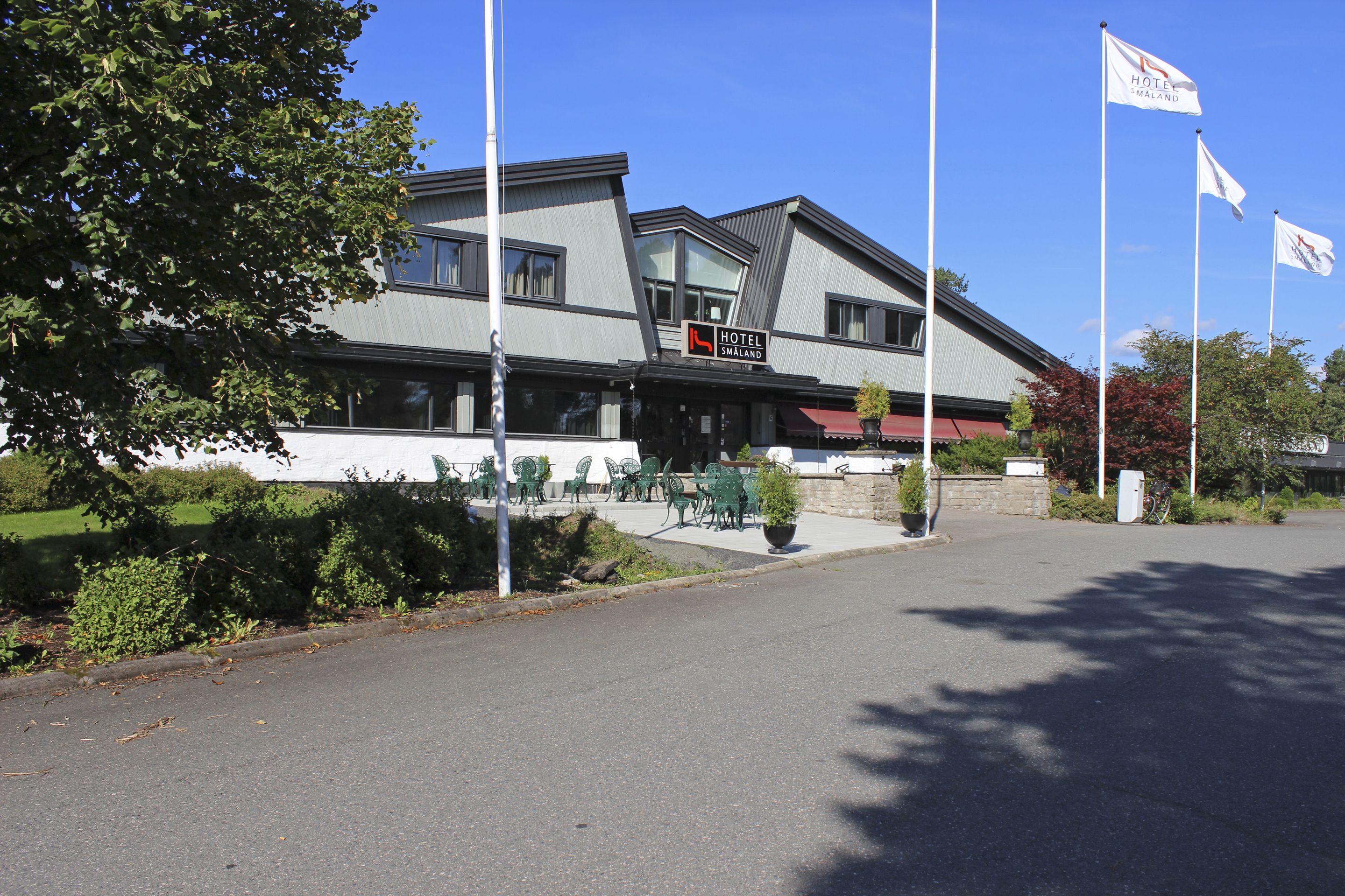 Ett hotell med en modern arkitektonisk design, som kännetecknas av en framträdande skylt, en uteservering och flera flaggor.