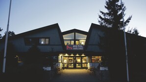 Un hotel con un diseño arquitectónico moderno, que destaca por una entrada imponente con puertas de cristal y un cartel que dice "HOTEL SMALAND".