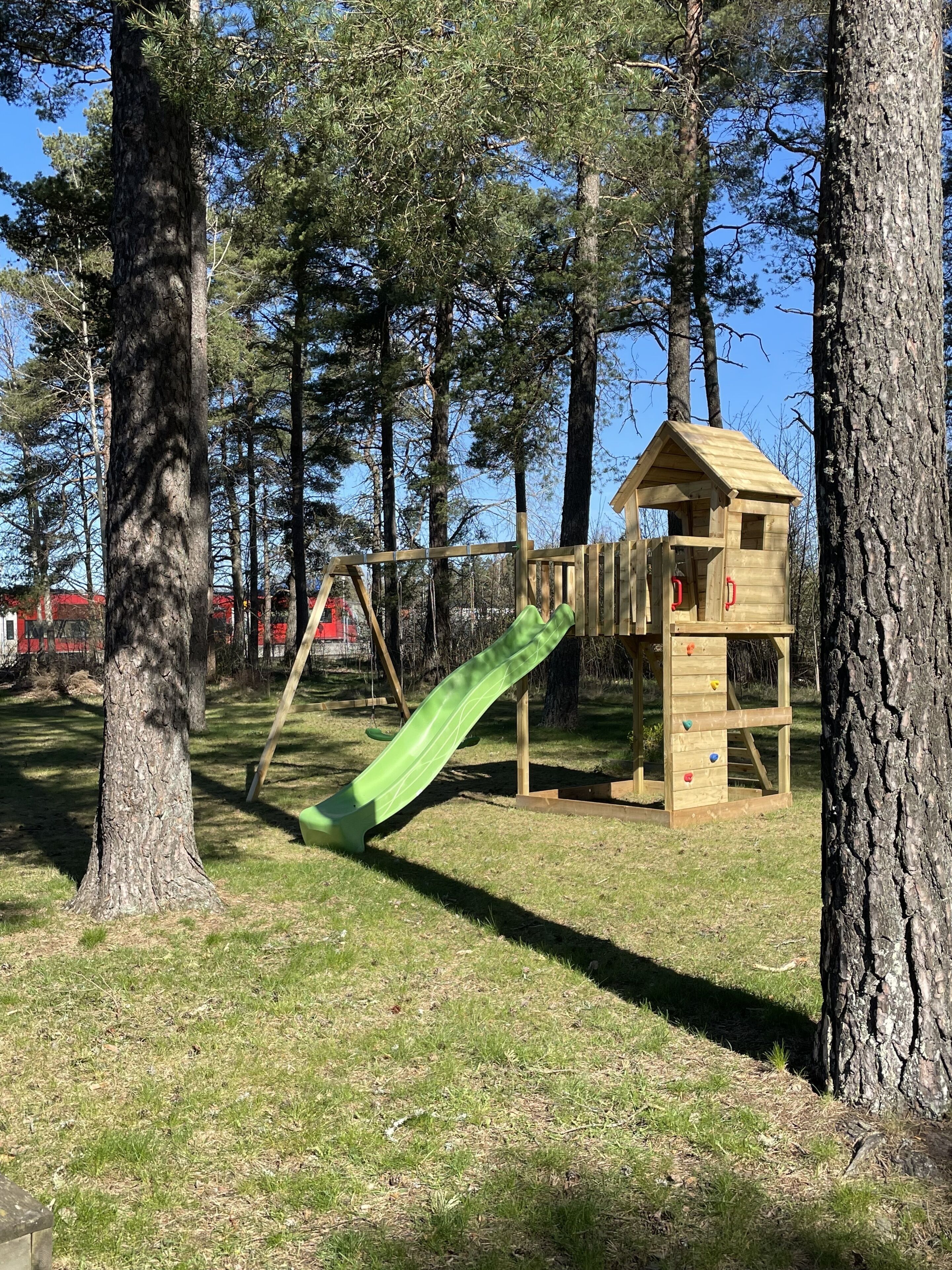 En lekplats med en rutschkana och en klättervägg, omgiven av träd.