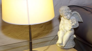 Uma luminária de mesa com cúpula branca e base metálica, posicionada ao lado de uma estátua branca de querubim sobre uma mesa de vidro.