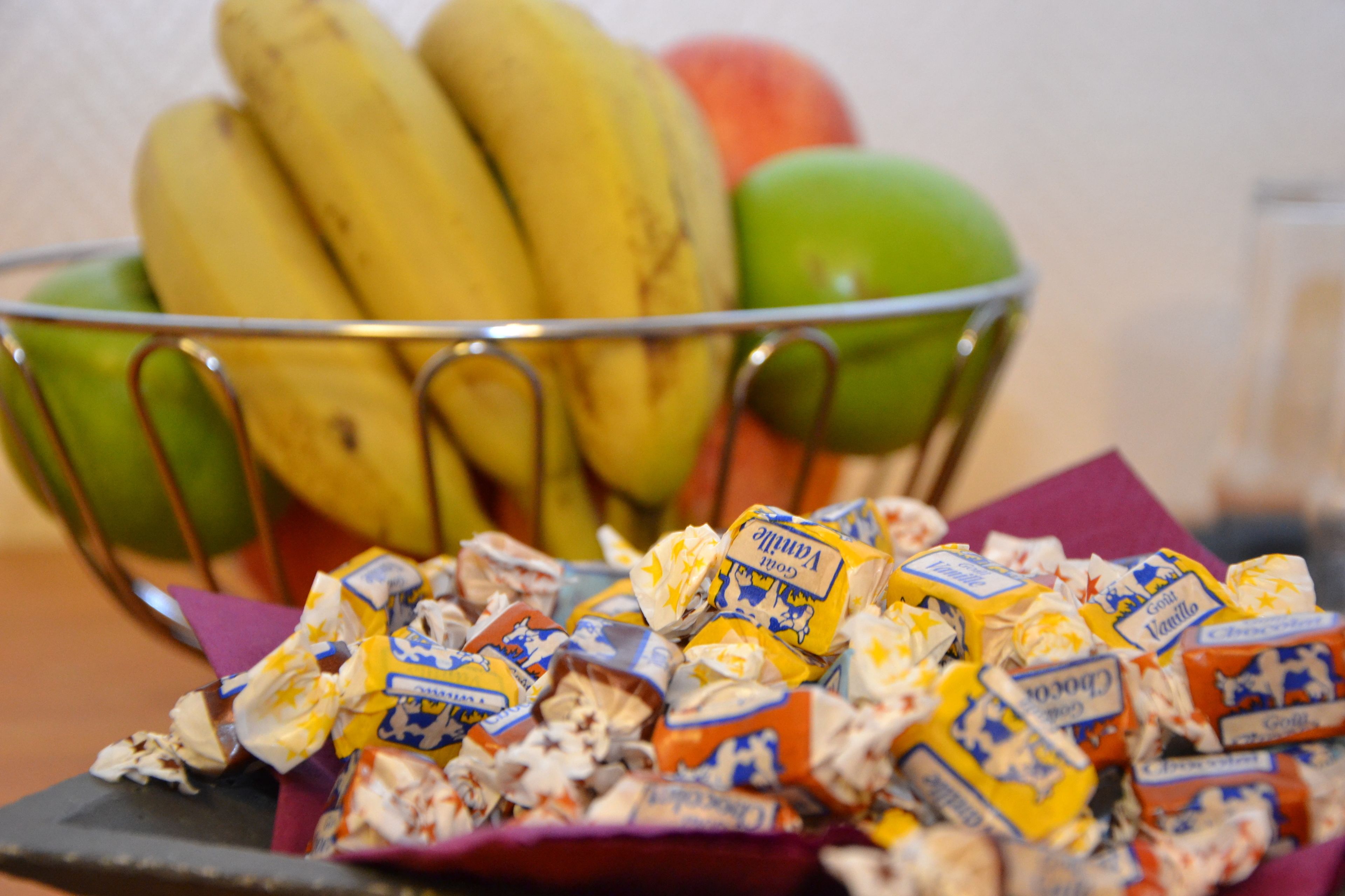 En metallskål som innehåller bananer och äpplen, med en hög chokladkakor framför.