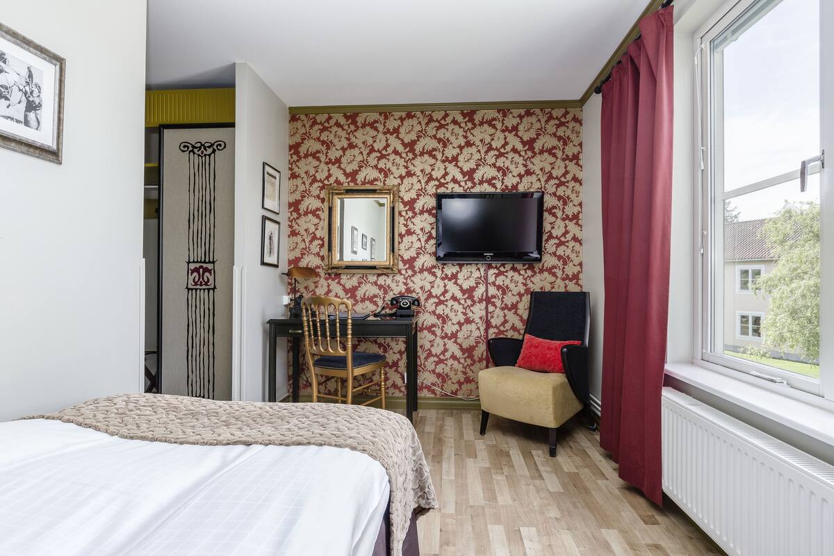 Habitación de hotel con una cama, un escritorio con silla, un televisor y una ventana con cortinas.