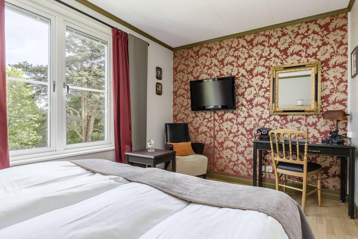 Una habitación de hotel con una cama, un escritorio, una silla, un televisor y una ventana con cortinas.