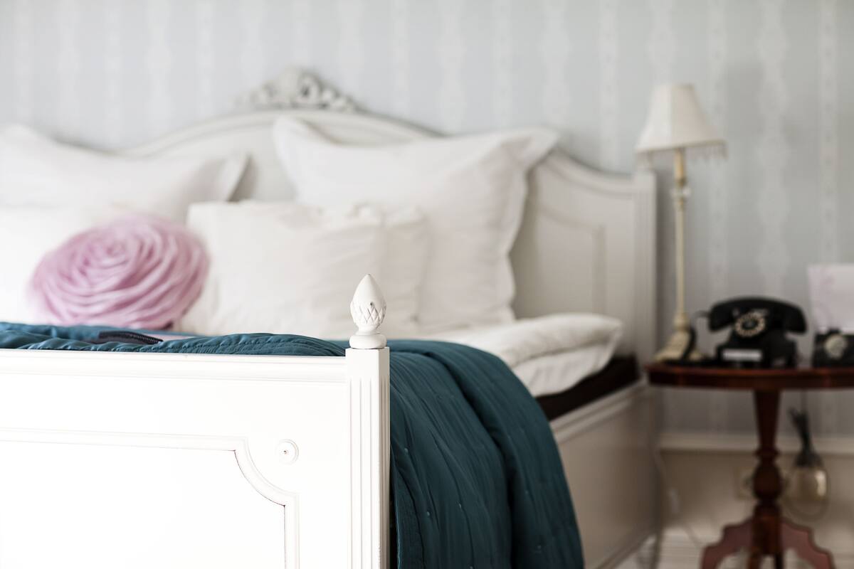Una cama bien hecha con un edredón verde azulado, almohadas blancas y una rosa rosa.