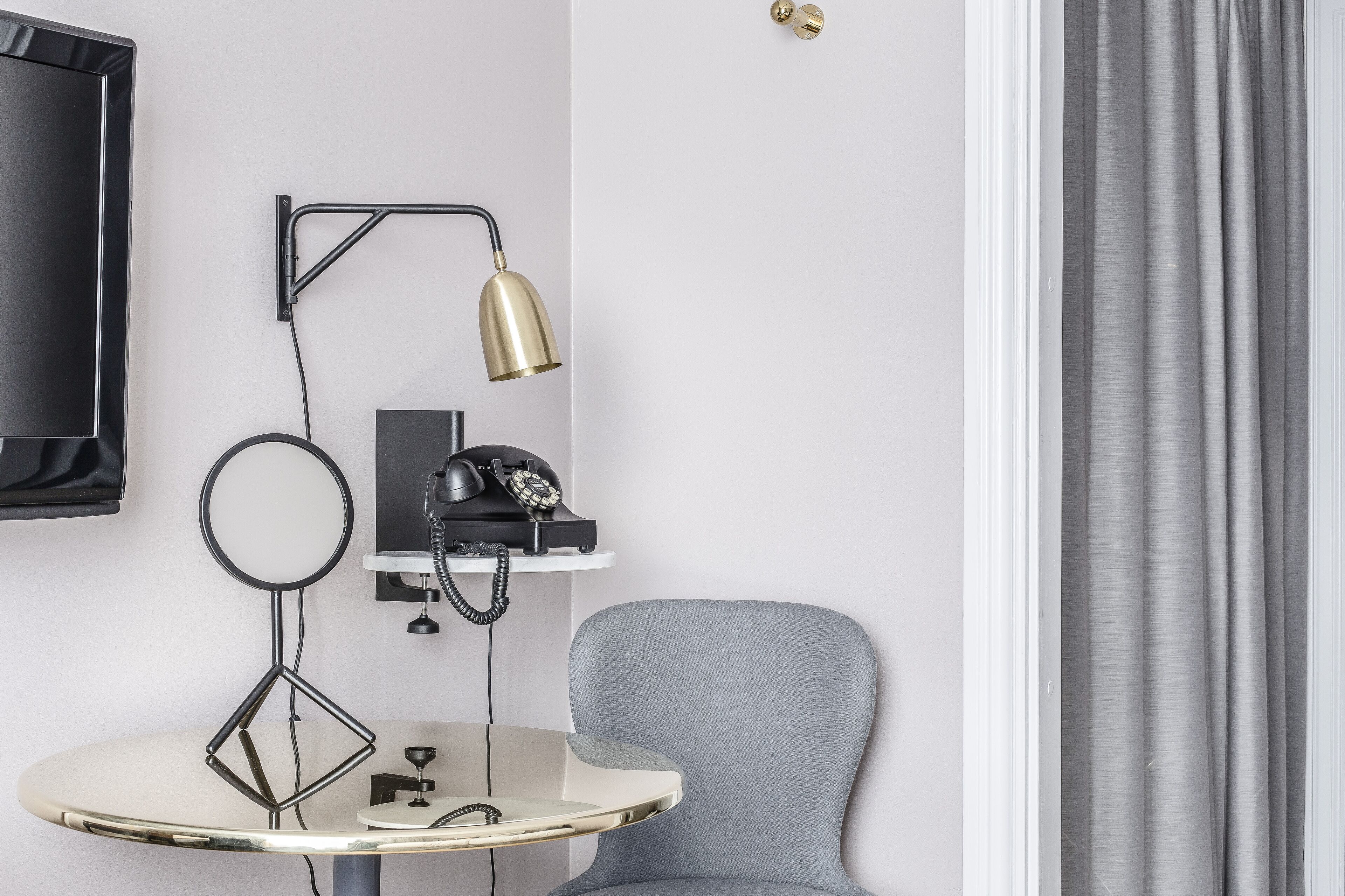 A modern room with a TV mounted on the wall, a desk with a lamp, a chair, and a telephone.