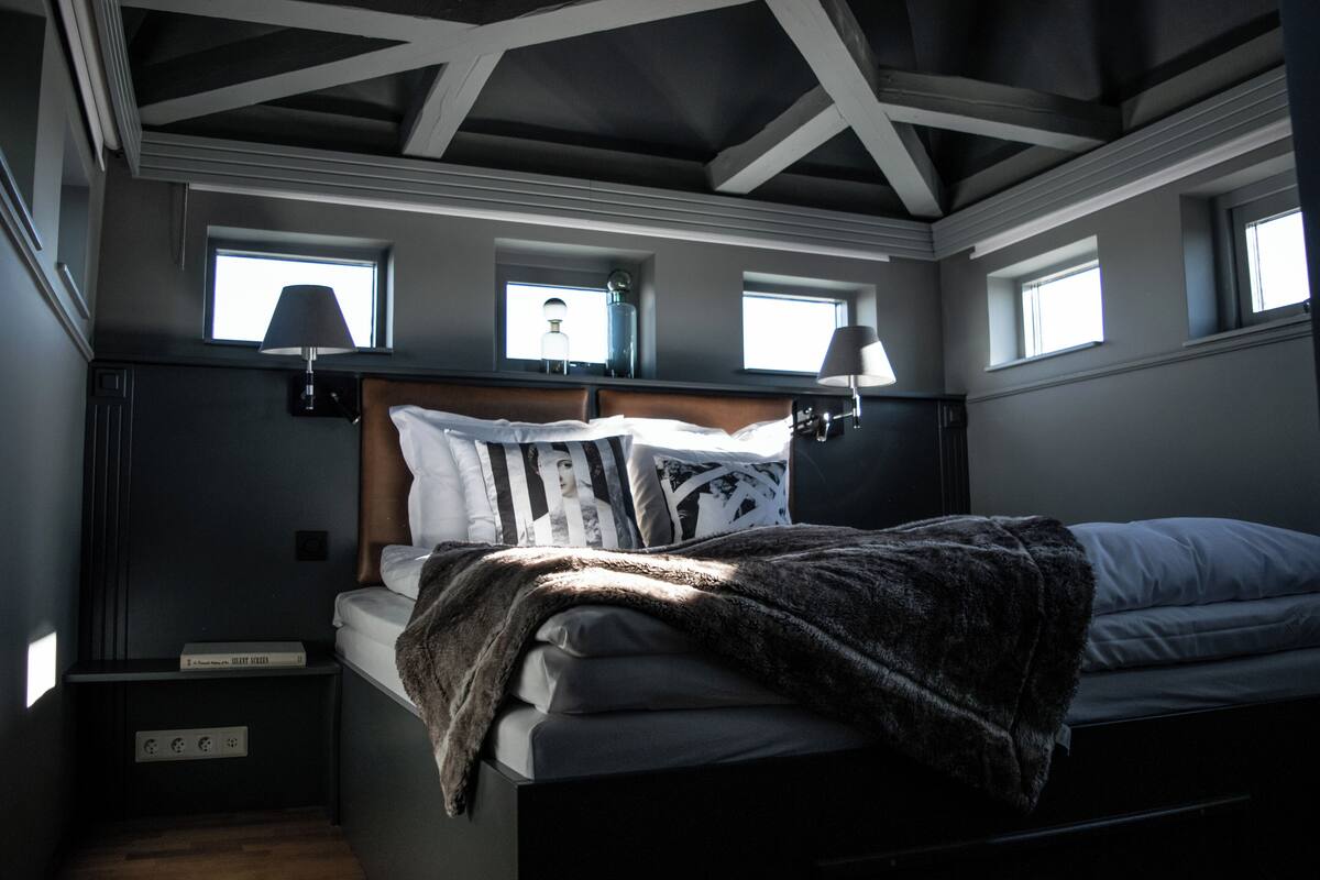 Un dormitorio con cama, mesita de noche, lámpara y ventana.