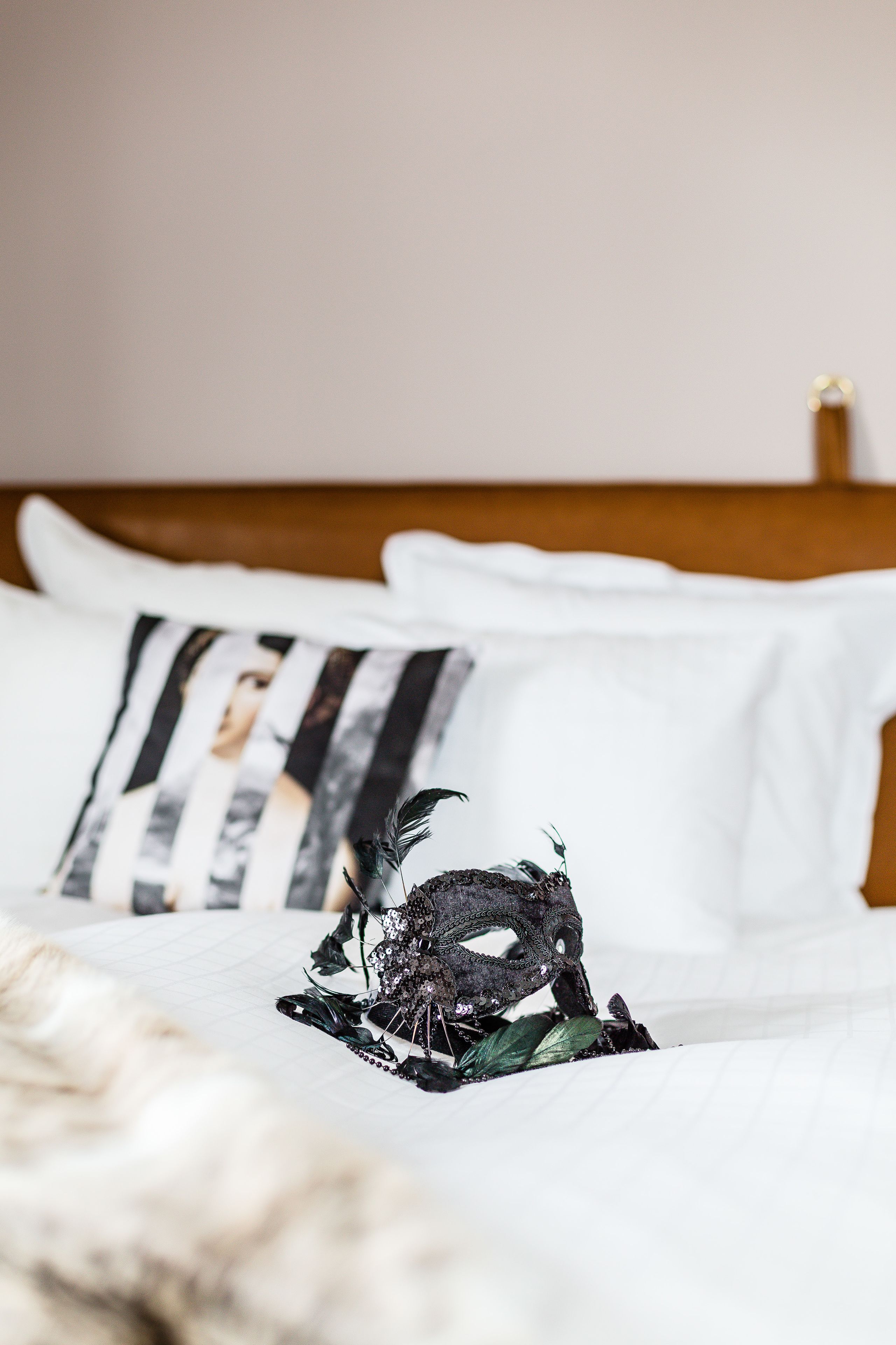 A neatly made bed with white linens, a black and white pillow, and a decorative black and white object on the bed.