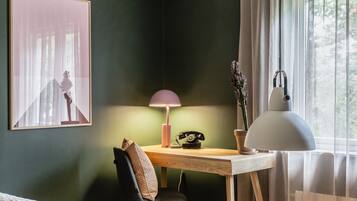 A room with a bed, a desk with a lamp, a telephone, and a framed picture on the wall.