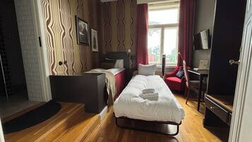 A hotel room with a bed, a desk, a chair, a TV, and a window with curtains.
