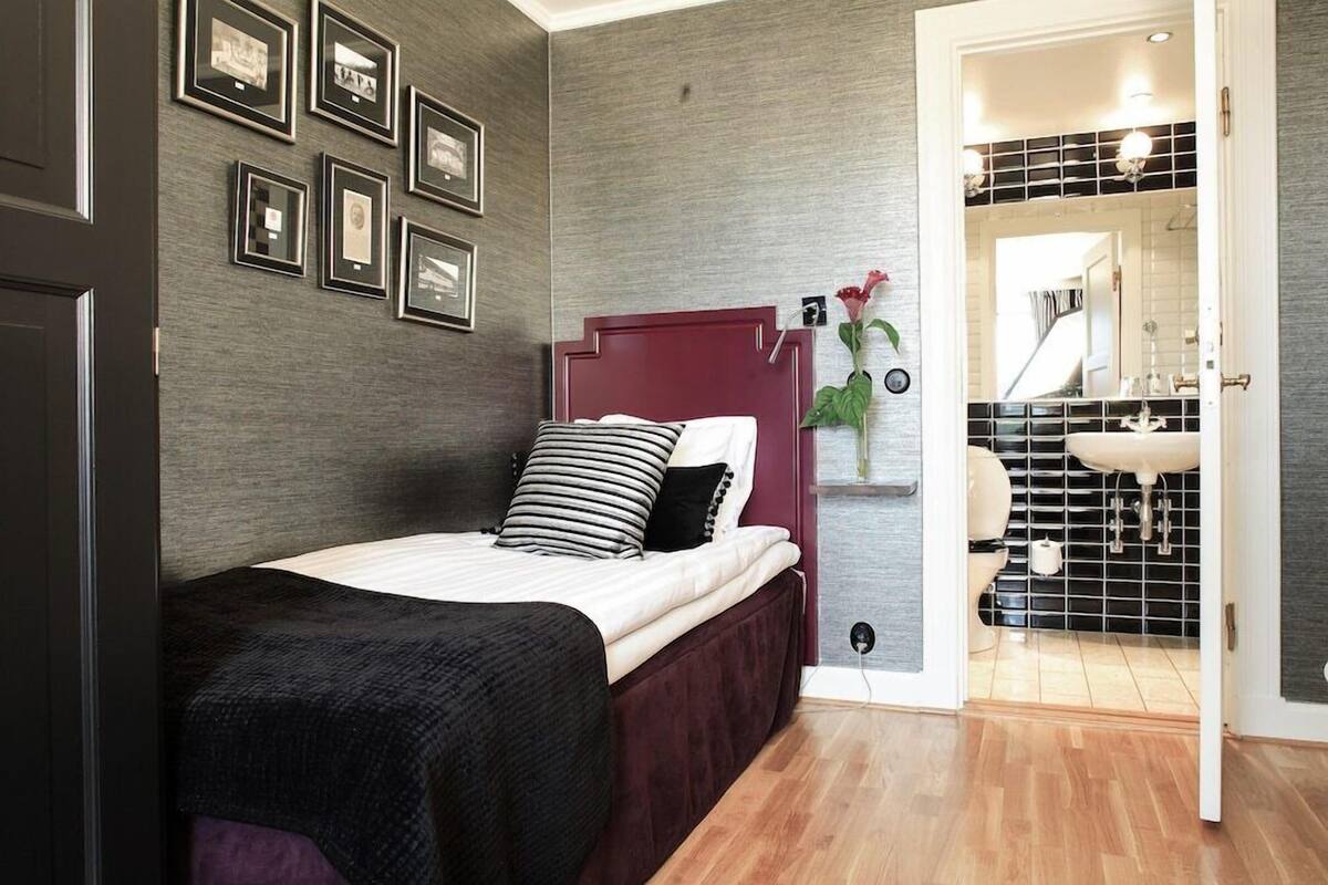 Un dormitorio con una cama, una mesita de noche, un reloj en la pared y una puerta que da al baño.