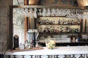 Uma área de bar com prateleiras de garrafas de bebidas, copos de vinho pendurados e uma exposição de café.