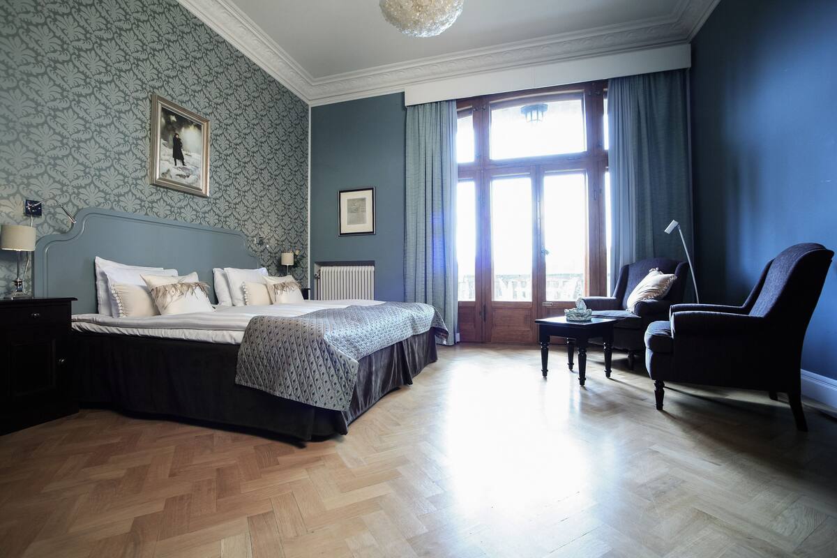 Un dormitorio con cama, una silla, una mesa y una ventana con cortinas.
