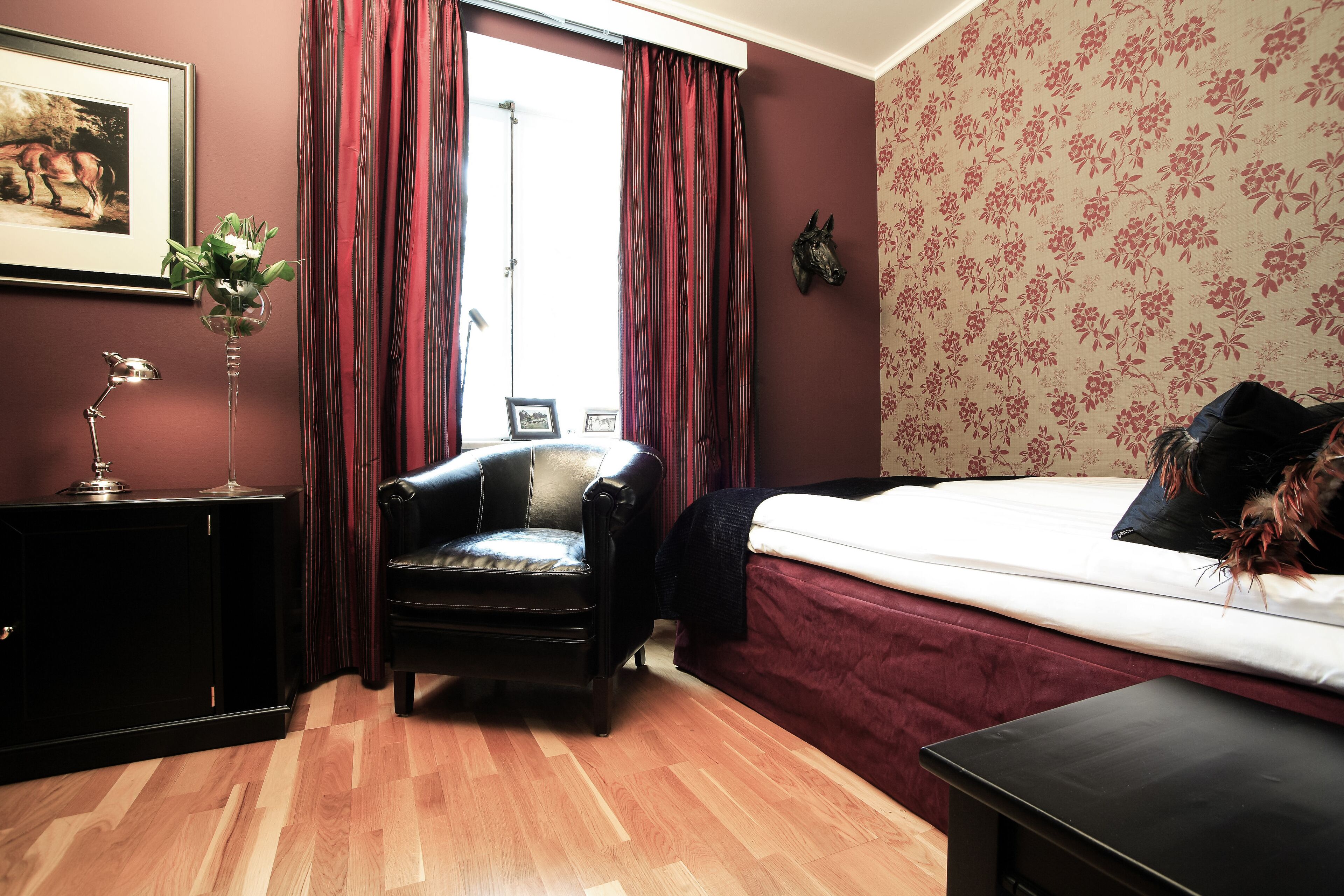A bedroom with a bed, a chair, a desk, and a window with curtains.