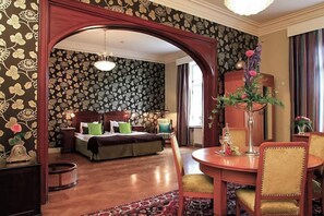Una habitación de hotel con una cama, un área de comedor con mesa y sillas, un arco de madera y un papel tapiz estampado.