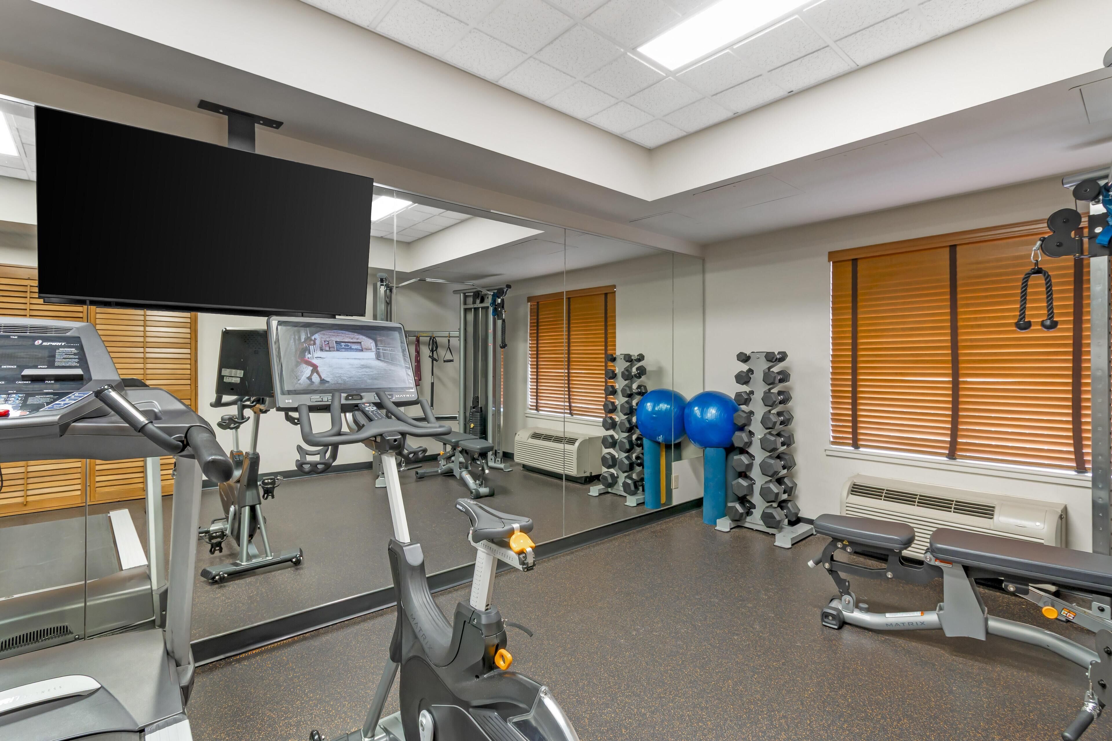 Un gimnasio con equipamiento de ejercicio, un televisor y un espejo.