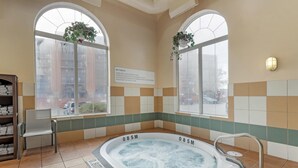 A hot tub with a sign indicating its depth, a chair, a shelf with towels, and large windows with plants. - Best Western Plus Pembina Inn & Suites (Winnipeg)