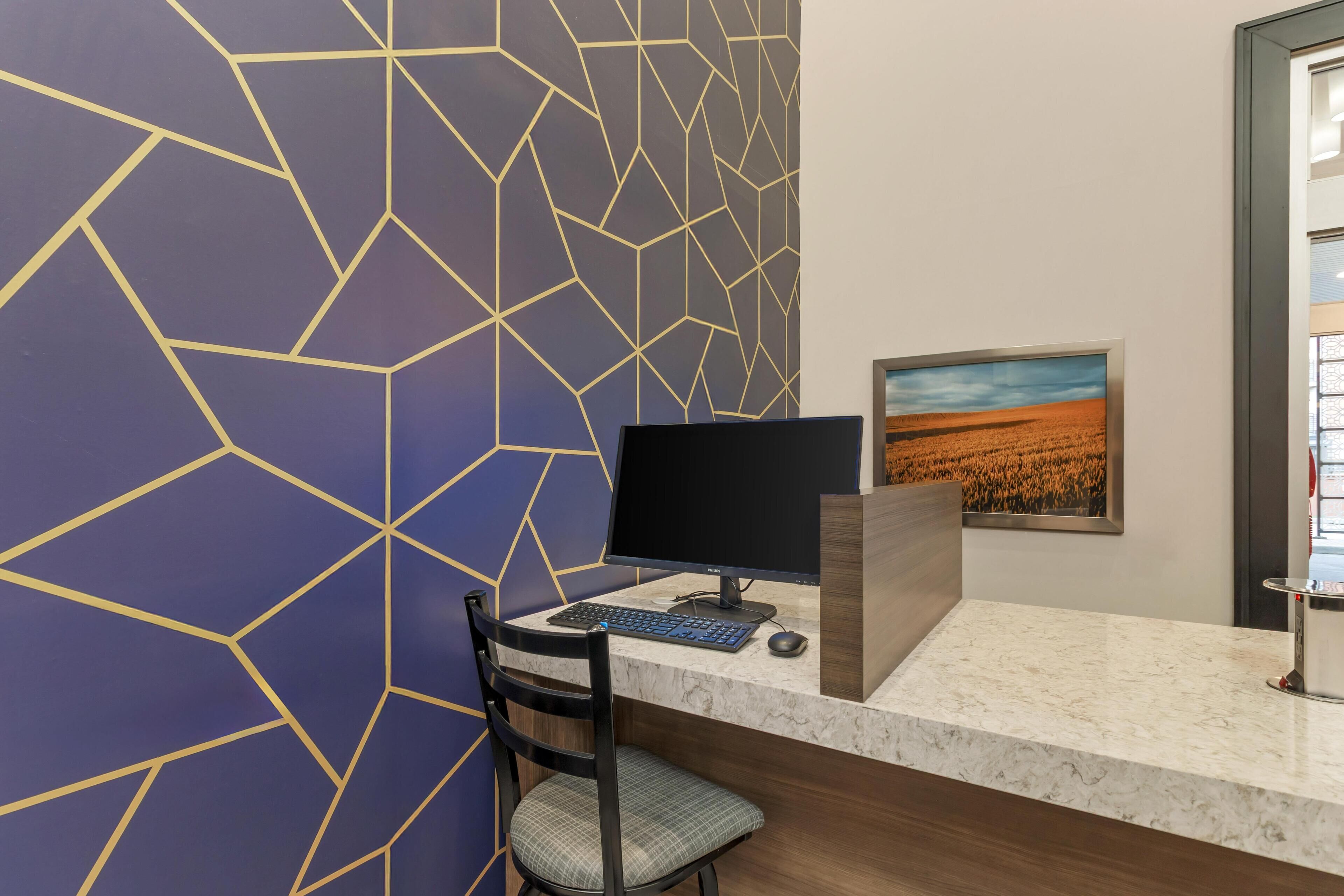 Un comptoir d’accueil avec un ordinateur, une chaise et un tableau représentant un paysage, accroché au mur.