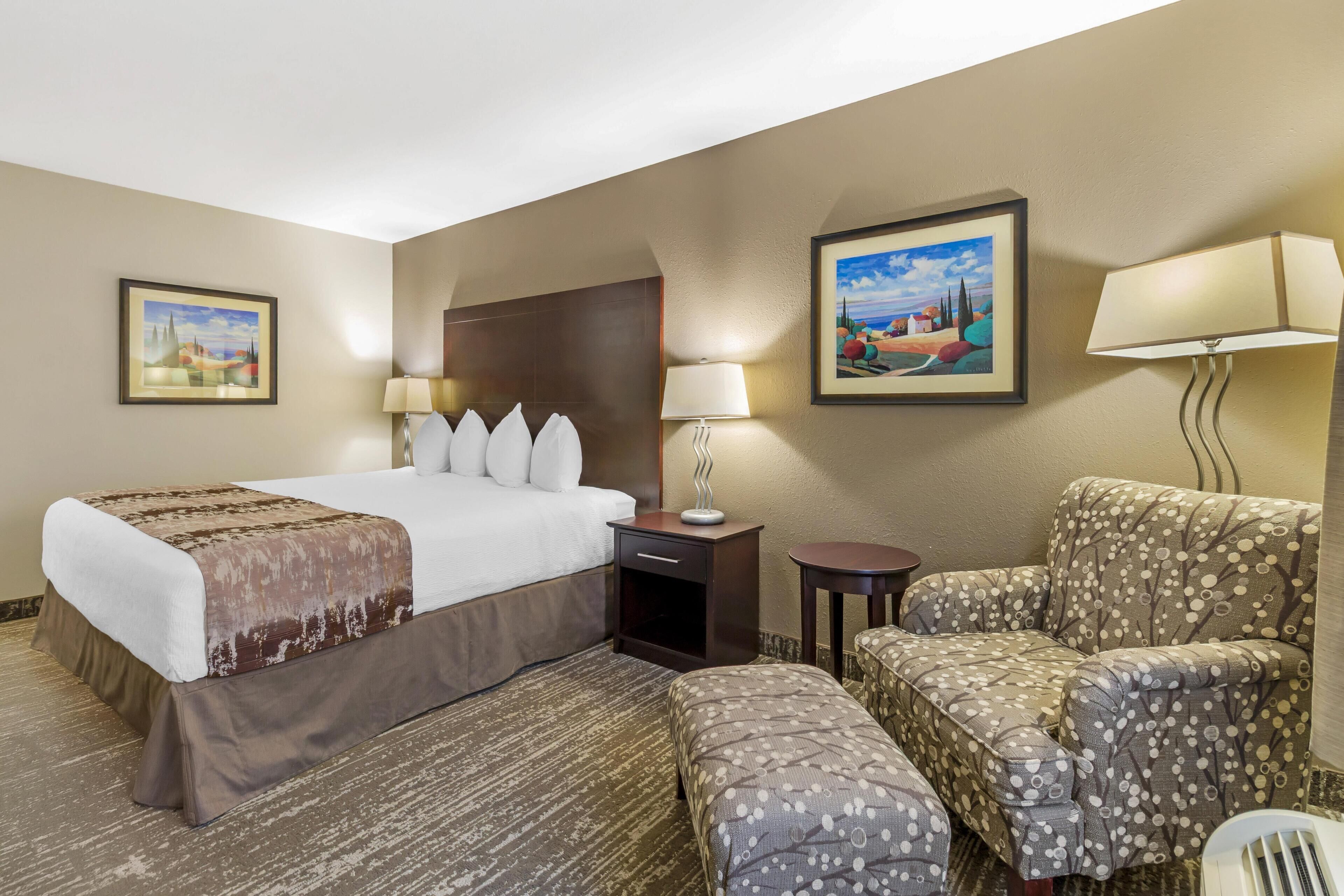 Una habitación de hotel con una cama, una silla, una mesita de noche y dos lámparas de pared.