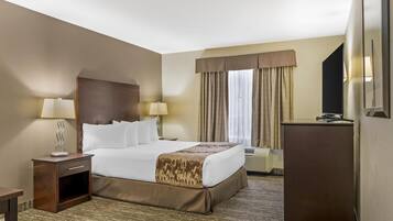 A hotel room with a large bed, two bedside tables with lamps, a desk, a chair, and a large window with curtains.