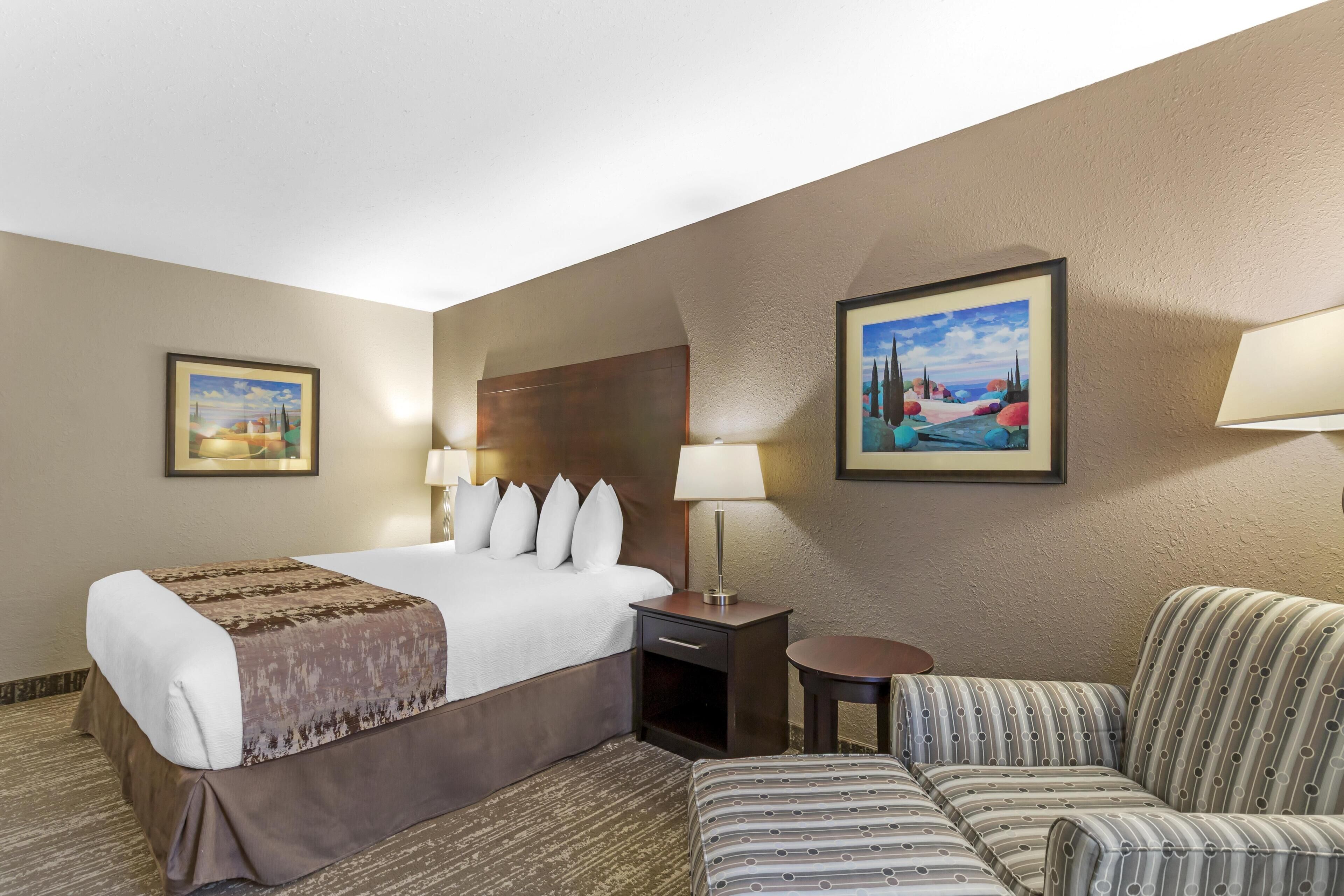 Habitación de hotel con una cama grande, un sofá, una mesita y dos lámparas de pared.