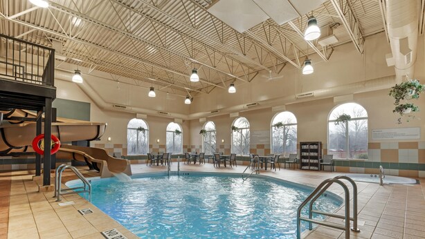 An indoor swimming pool with a slide, seating area, and safety signage. - Best Western Plus Pembina Inn & Suites (Winnipeg)
