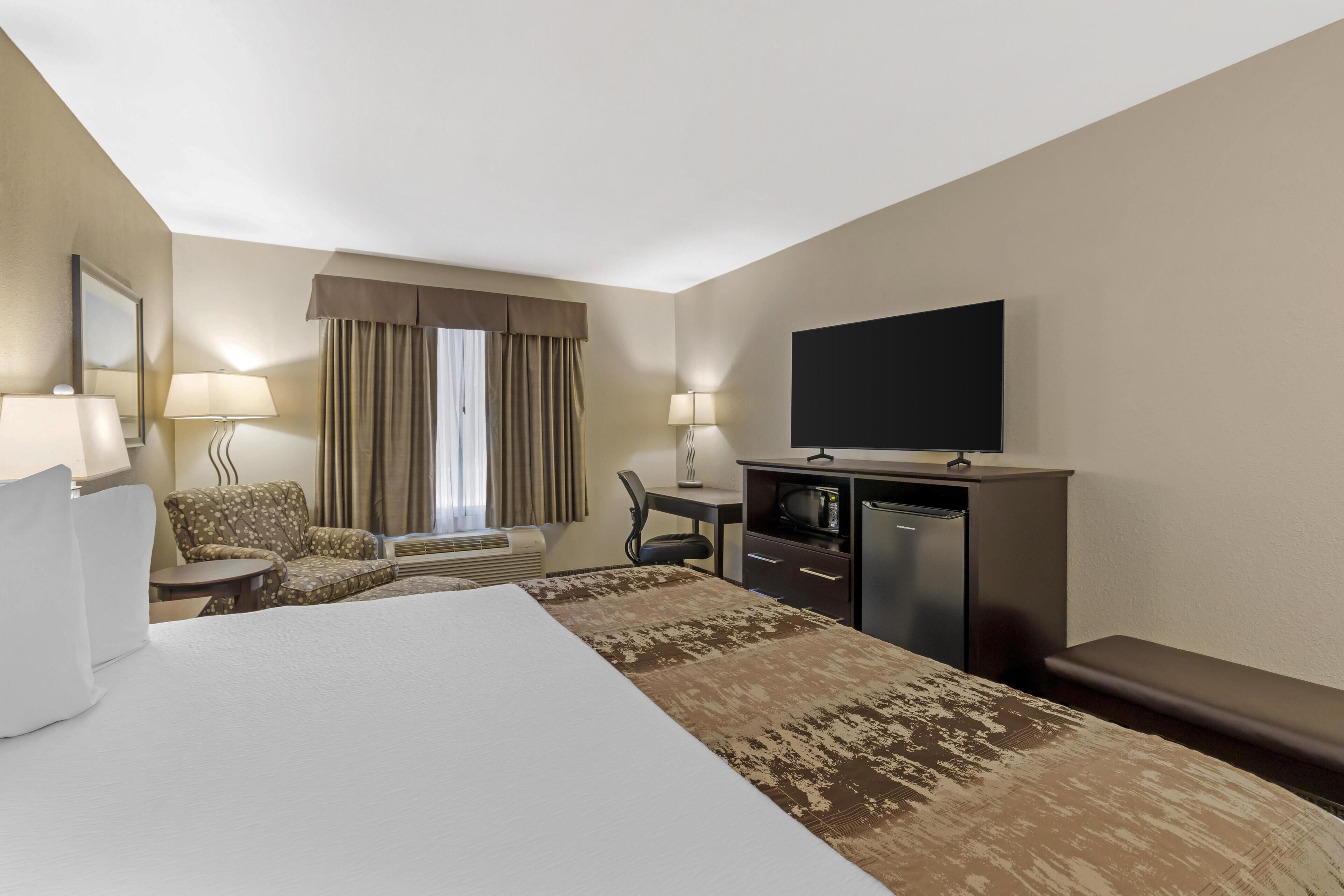 Habitación de hotel con una cama grande, un escritorio con televisor de pantalla plana, una silla, una mesita pequeña y un banco.