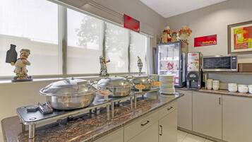 A buffet setup with multiple serving stations, a coffee machine, and a refrigerator.