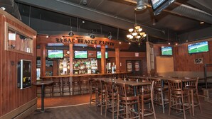 A bar area with wooden walls, multiple TVs, and a bar counter. - Burntwood Hotel (Thompson)
