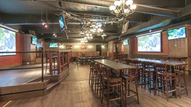 A spacious restaurant with multiple tables and chairs, a stage for presentations, and several screens displaying content. - Burntwood Hotel (Thompson)