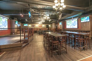 A spacious restaurant with multiple tables and chairs, a stage for presentations, and several screens displaying content. - Burntwood Hotel (Thompson)