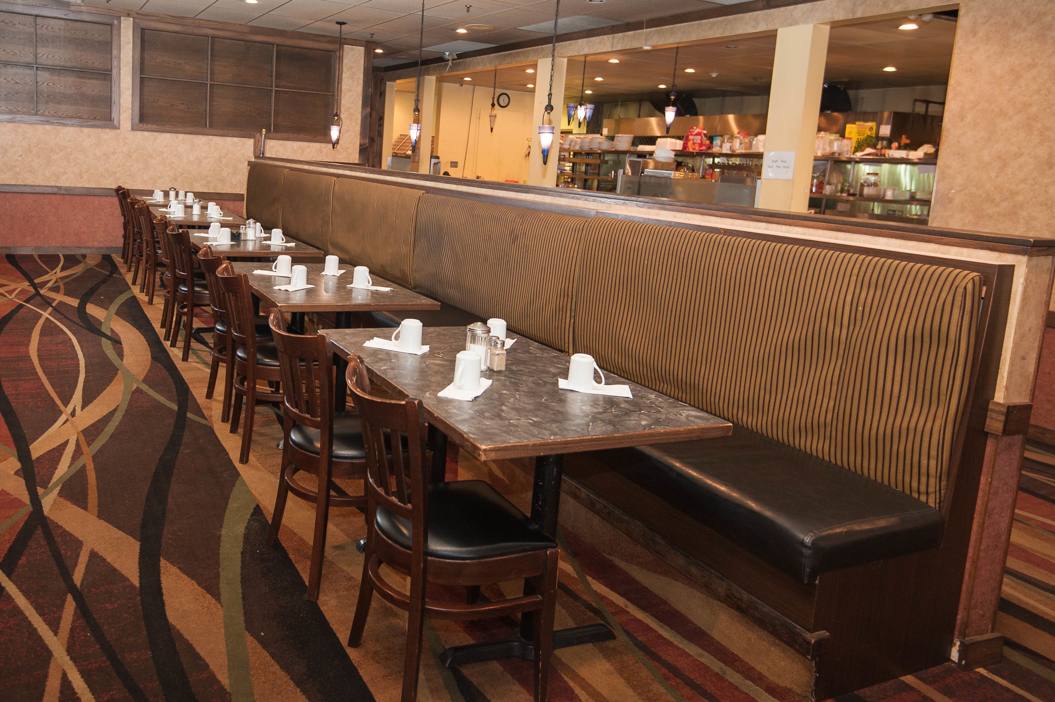 Un restaurante con varias mesas y cabinas, un suelo estampado y vistas a la cocina a través de un separador de vidrio.