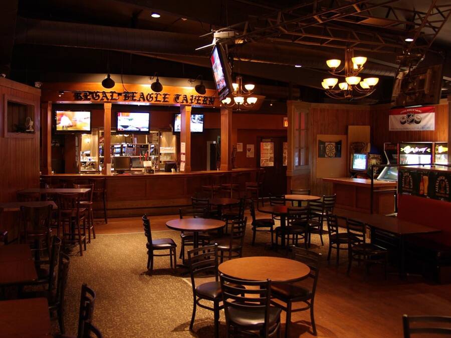 A restaurant interior with wooden decor, multiple tables and chairs, a bar area, and televisions on the walls.