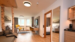 A modern hotel room with a wooden floor, a bed, a desk, a chair, a sofa, a TV, and a large mirror. - Alpenhof Oberstdorf Hotel & Spa, BW Signature Collection (Oberstdorf)