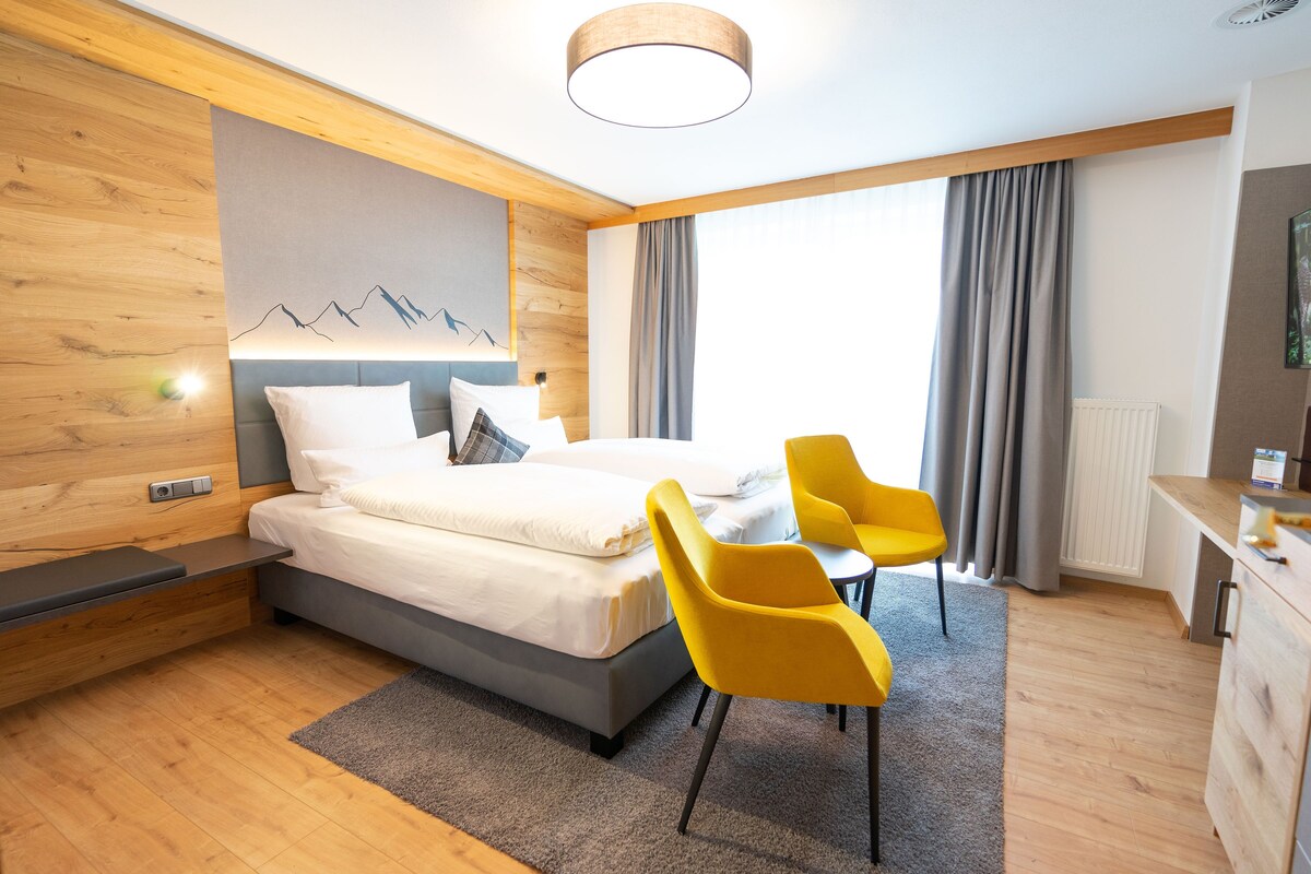 A modern hotel room with a bed, a desk, and a chair.