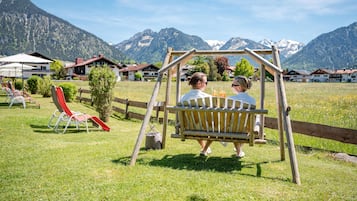 A couple on a swing in a grassy area with a mountain backdrop.