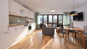 A modern kitchen with white cabinets, a wooden countertop, and a dining area with a wooden table and chairs. - Alpenhof Oberstdorf Hotel & Spa, BW Signature Collection (Oberstdorf)