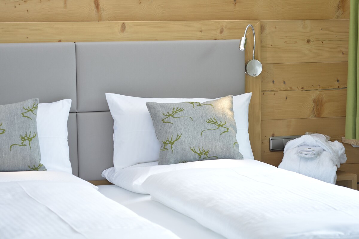 A neatly made bed with white bedding and grey pillows with green patterns, a wooden headboard, and a visible power outlet.