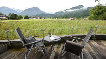 A deck with two chairs and a table, overlooking a field with mountains in the background.