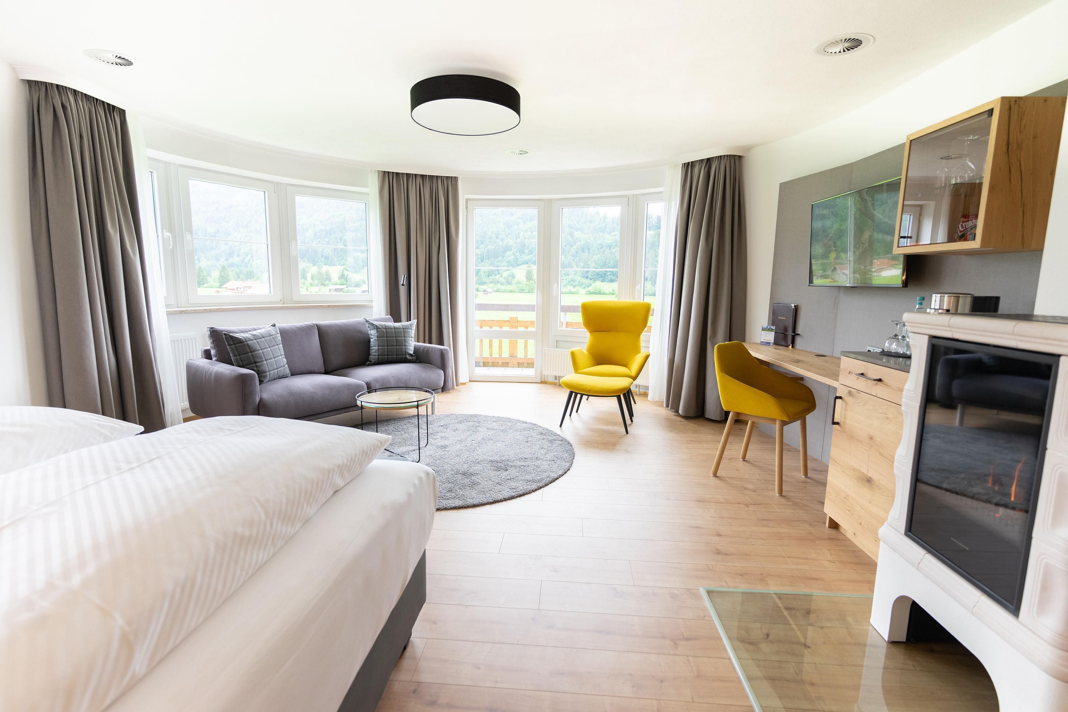 Una habitación de hotel moderna con cama, sofá, dos sillones, escritorio y chimenea.