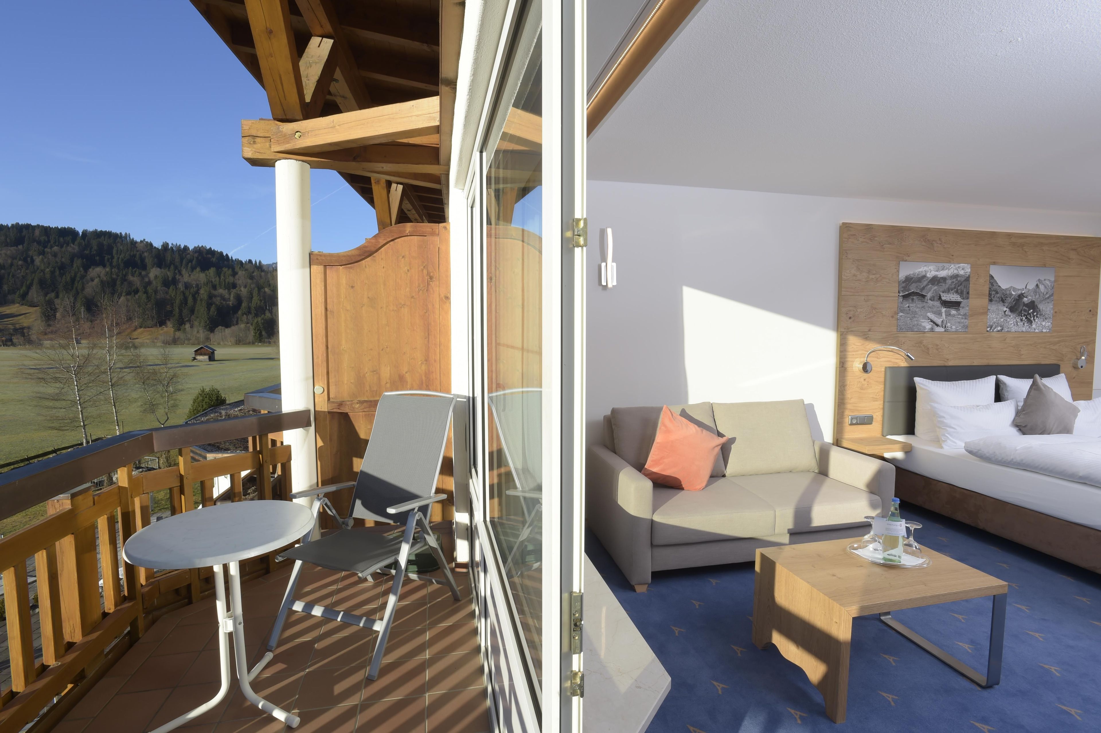 Un balcone con ringhiera in legno, una porta vetrata che dà su una stanza con un divano, un tavolino da caffè e un letto.