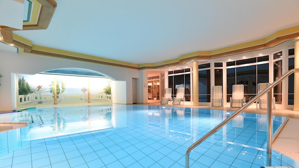 A large indoor swimming pool with clear blue tiles, a staircase leading to a balcony, and a view of a landscaped area through large windows. - Alpenhof Oberstdorf Hotel & Spa, BW Signature Collection (Oberstdorf)