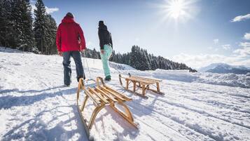 Two people walking on a snow-covered path with benches and trees in the background.