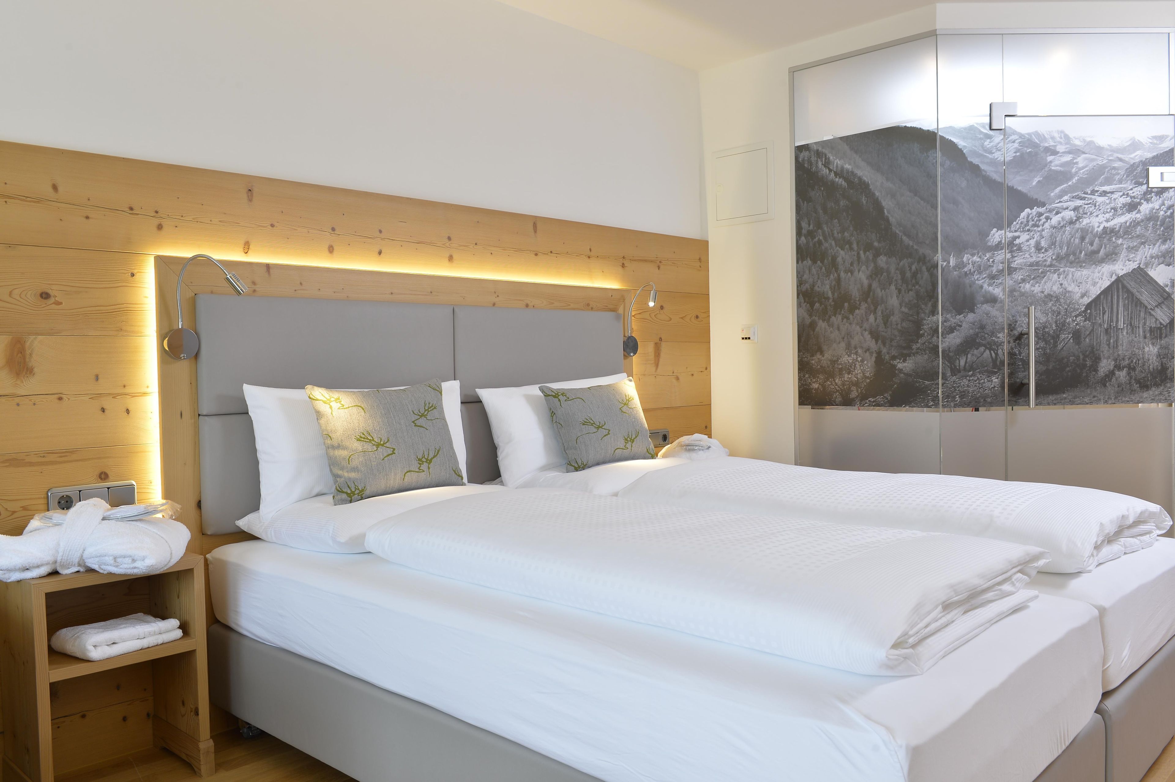 Ein Hotelzimmer mit hölzernem Kopfteil, einem großen Bett mit weißer Bettwäsche, einem Nachttisch mit Handtüchern und einer Wandleuchte.