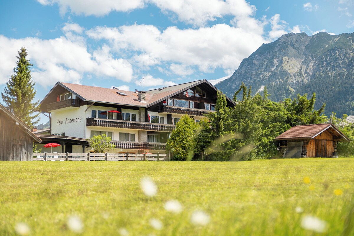 A two-story building with a balcony, surrounded by a grassy field and mountains in the background.
