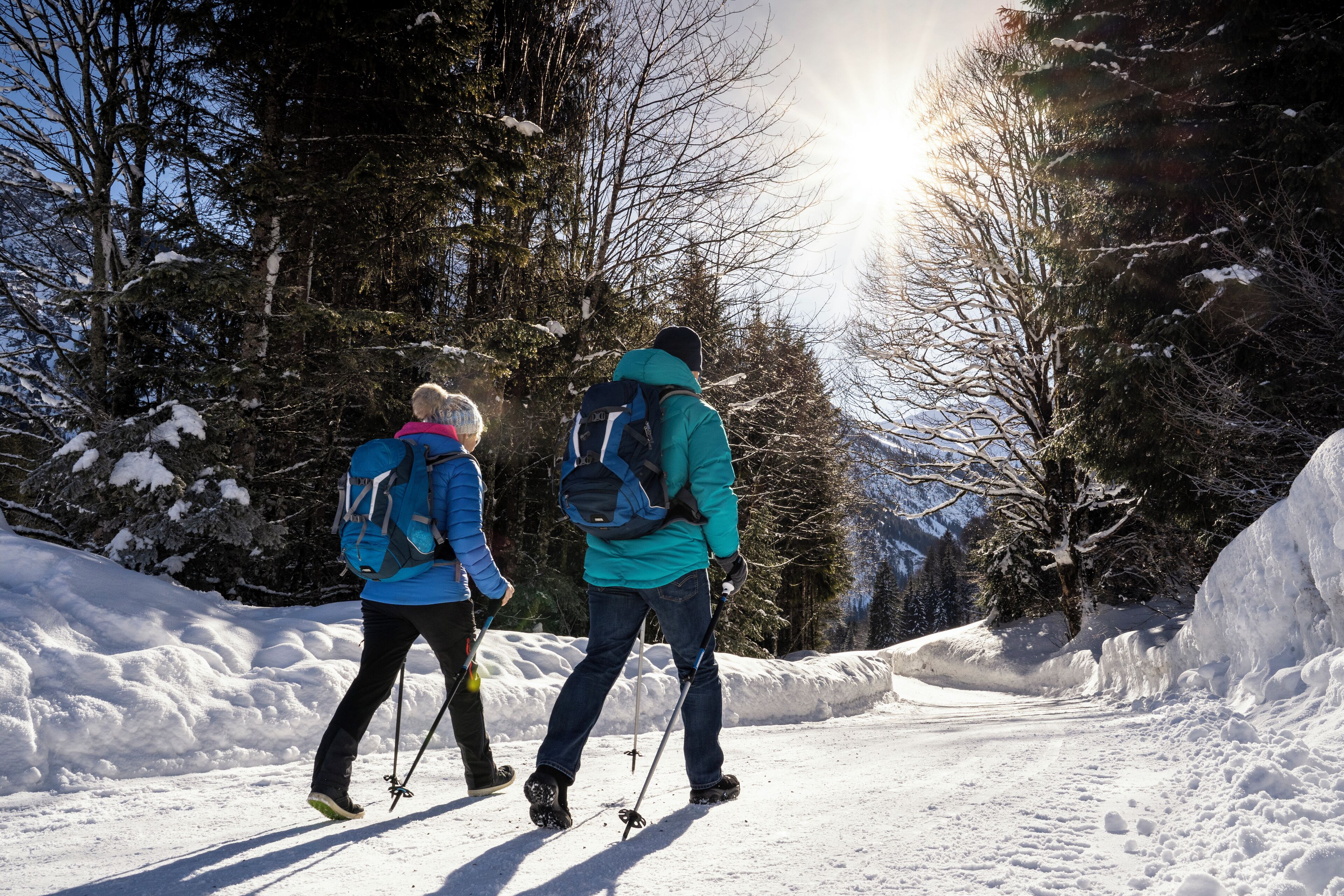 Dos personas caminando en un bosque nevado con árboles y cielo despejado.