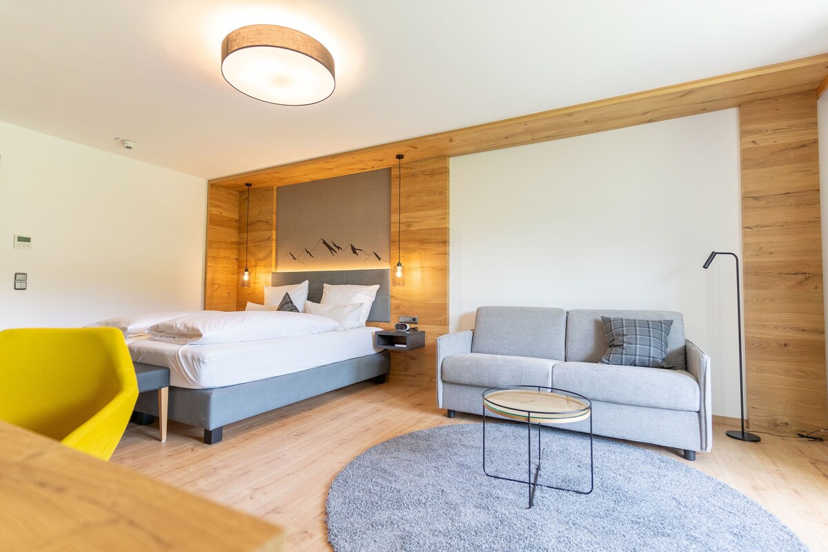 A modern hotel room with a bed, a sofa, a small table, and a chair.