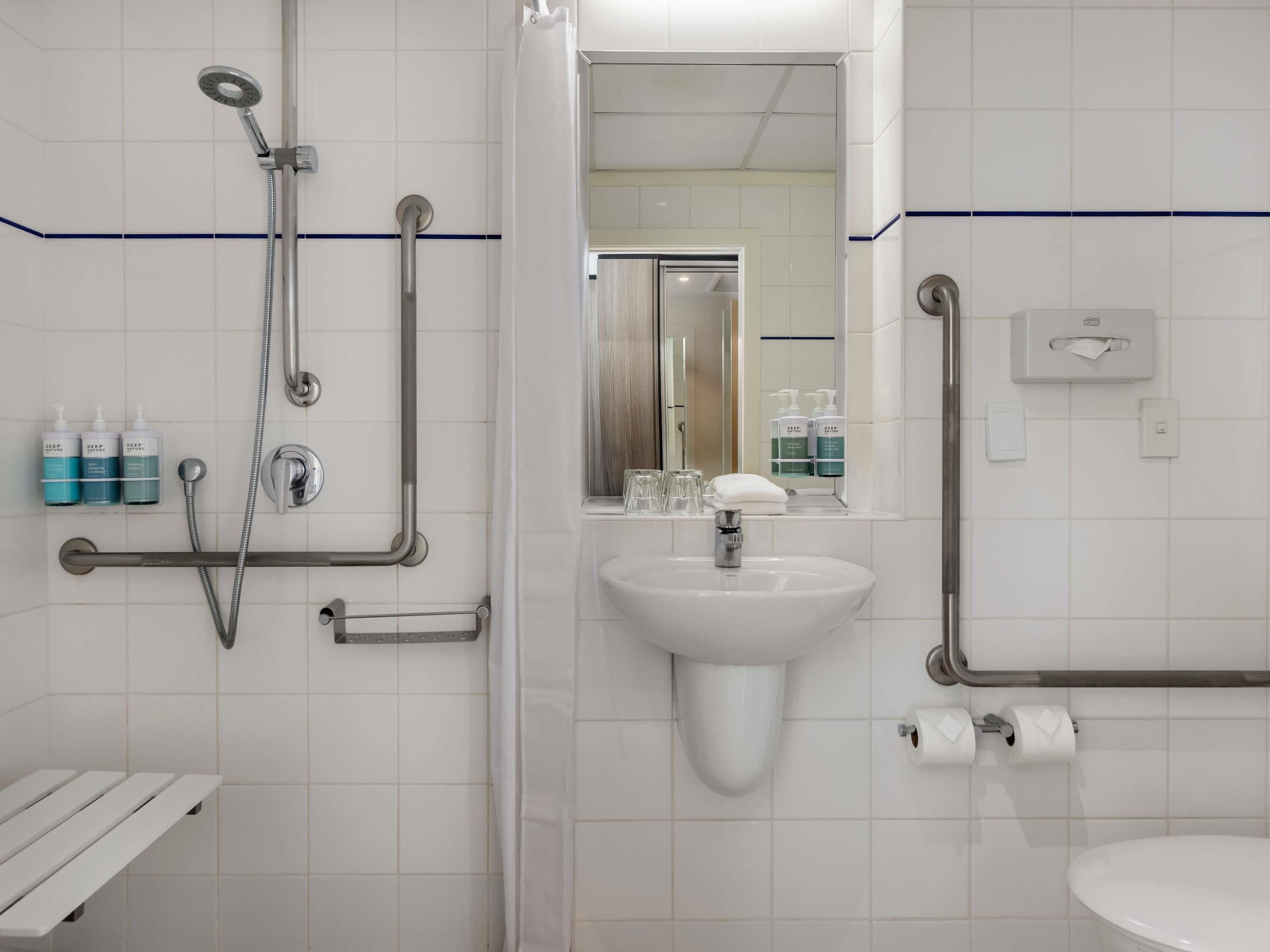 Une salle de bain équipée d’une douche, d’un lavabo, de toilettes et de barres d’appui.
