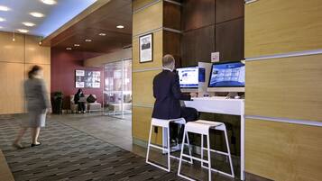 A modern reception area with a wooden panel wall, a desk with a computer, and a seating area with a glass partition.