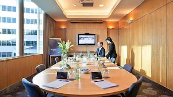 Un salón de conferencias con una larga mesa, sillas, una pantalla de proyector y un ventanal grande.