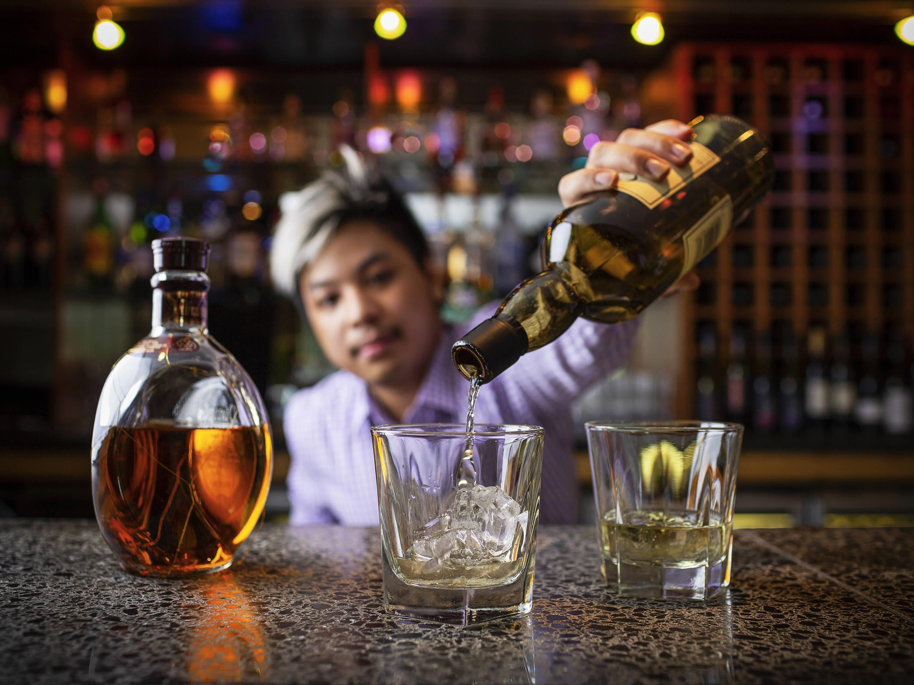 A person pouring a liquid from a bottle into a glass with ice.